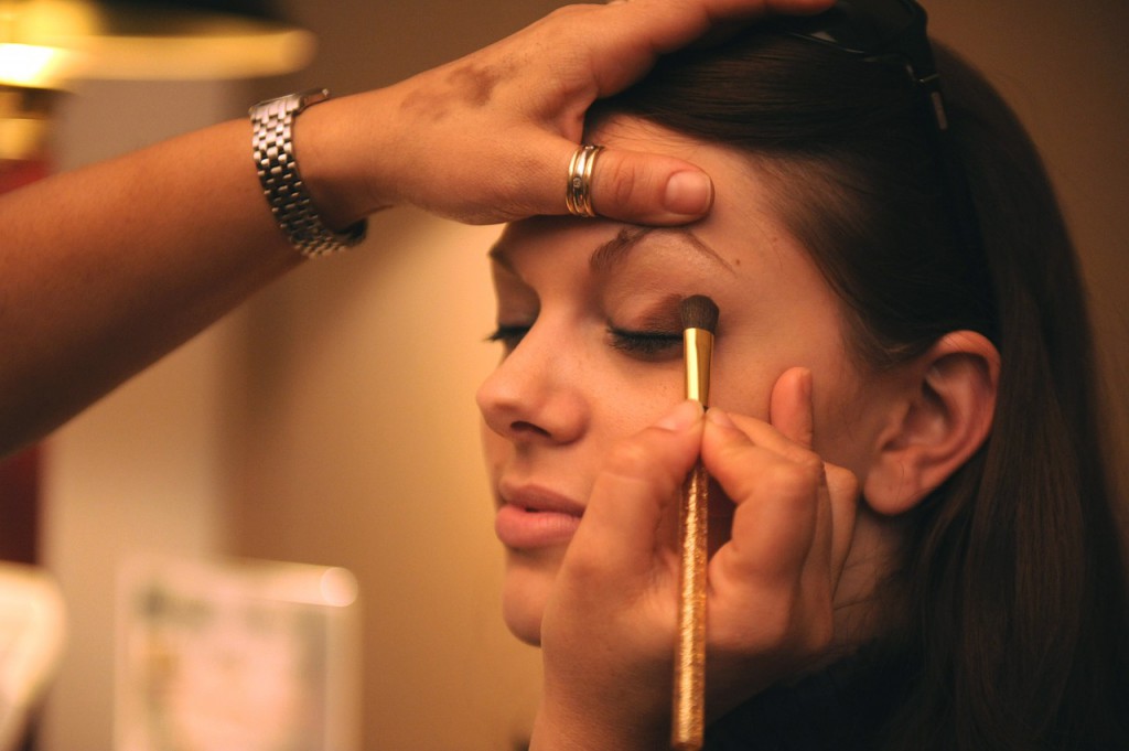 Makeup - A young beautiful woman sitting down while another woman applies mascara to her face inside a spa room